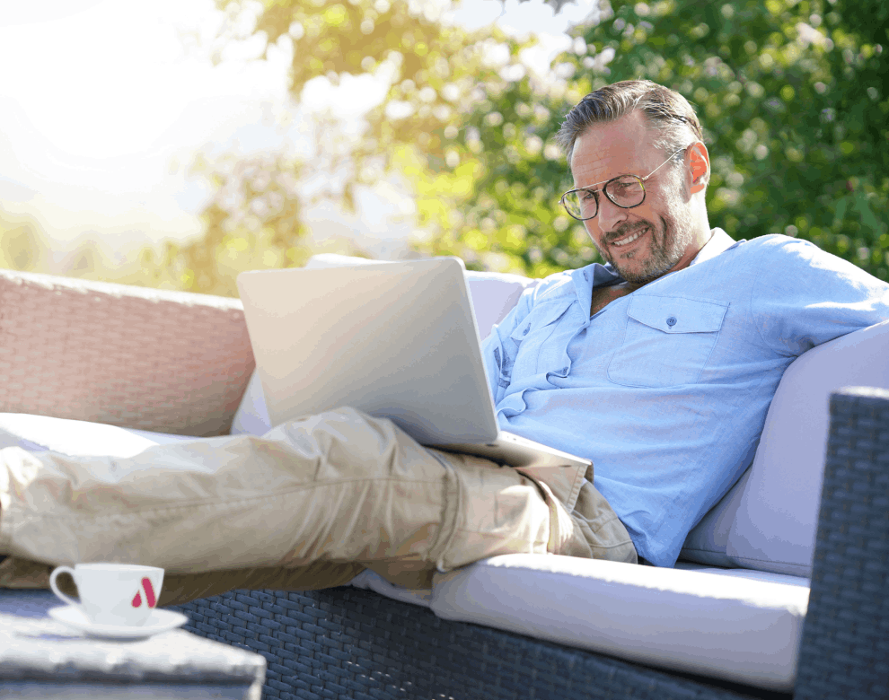 Mann sitzt gemütlich mit Laptop auf einer Terrasse  