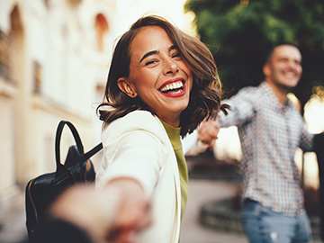 Eine Frau blickt über ihre rechte Schulter und lacht in die Kamera.