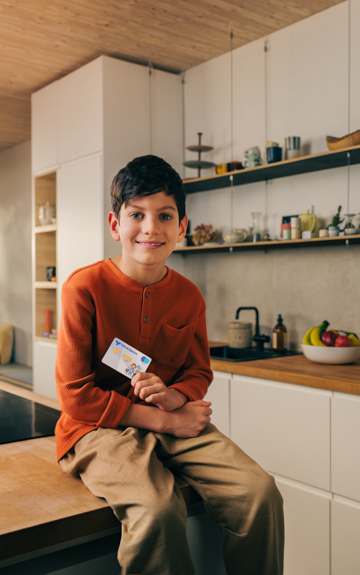Ein Bub sitzt auf einem Tisch in der Küche und hält eine Volksbank Jugend Sparkarte in der Hand.
