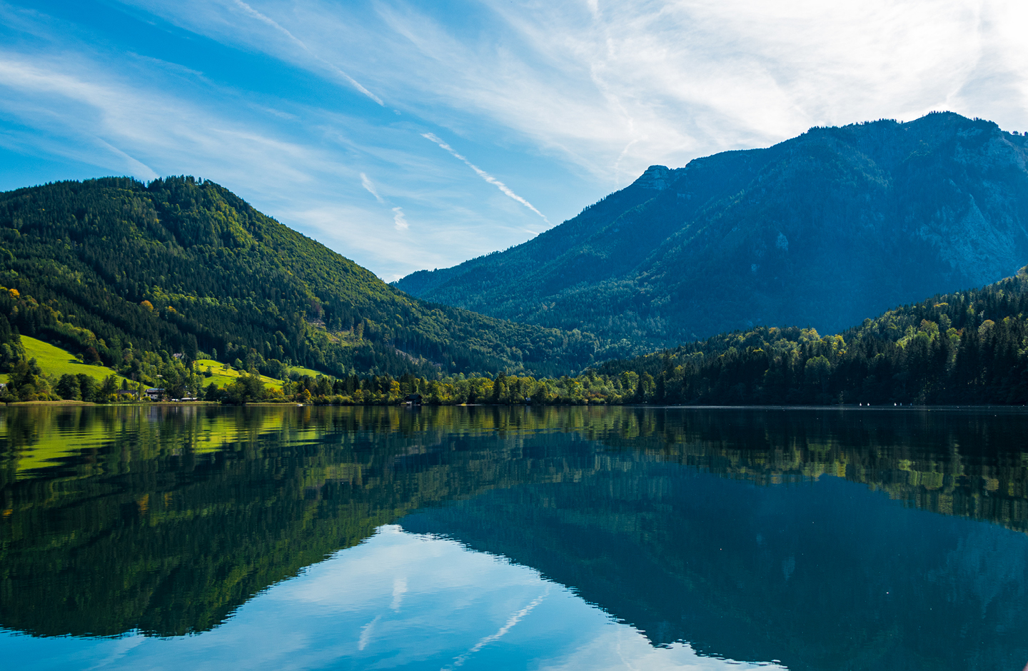 Im Vordergrund ein See, dahinter grün bewaldete Berge.