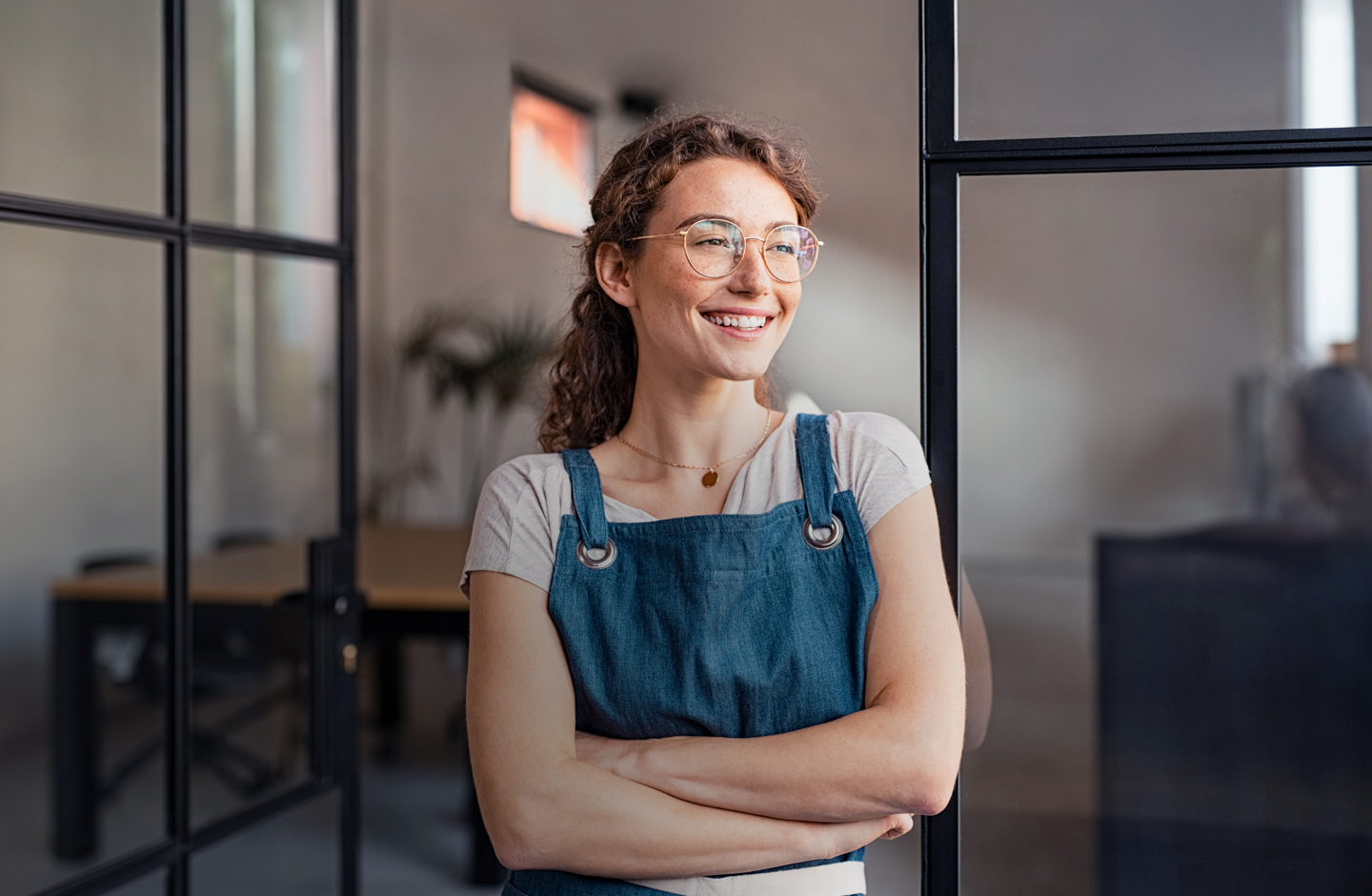 Eine Dame mit blauer Schürze steht zufrieden in ihrem Büro.